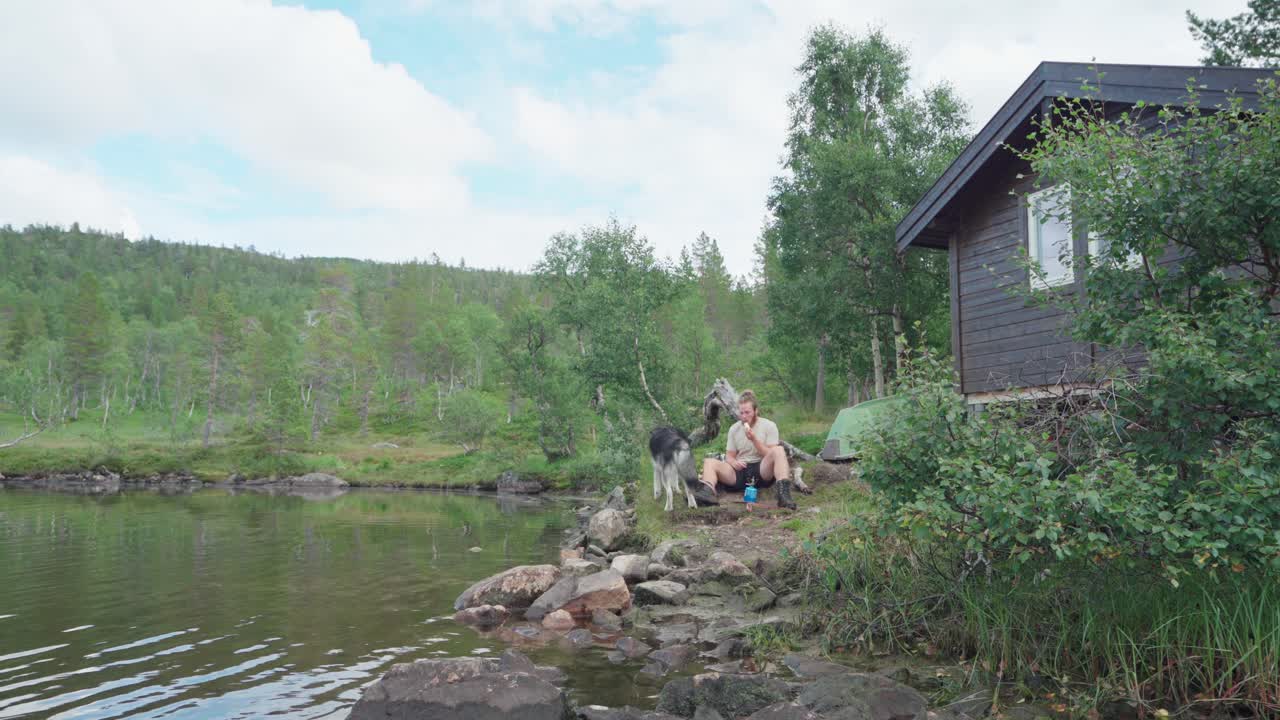 мужчина со своей собакой породы аляскинский маламут сидит и отдыхает на берегу реки в андердалене, сенья, норвегия