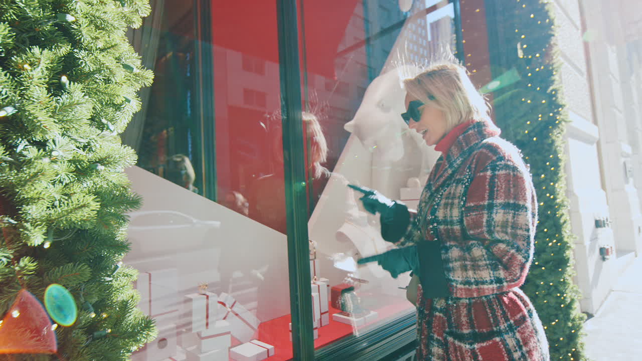 New York, USA, 2 aprile 2026: Donna in cappotto a quadri che guarda una vetrina delle feste. Inquadratura di profilo di una donna in capospalla a quadri che osserva la vetrina di un negozio di lusso con una statua di pantera bianca a New York