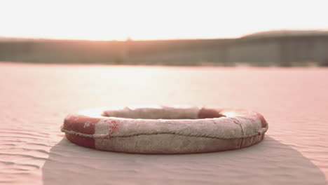 old lifebuoy on sandy beach at sunset