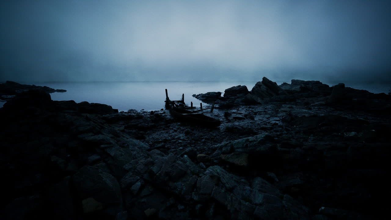 Mysterious boat remains on a rocky shore under a foggy twilight sky ...