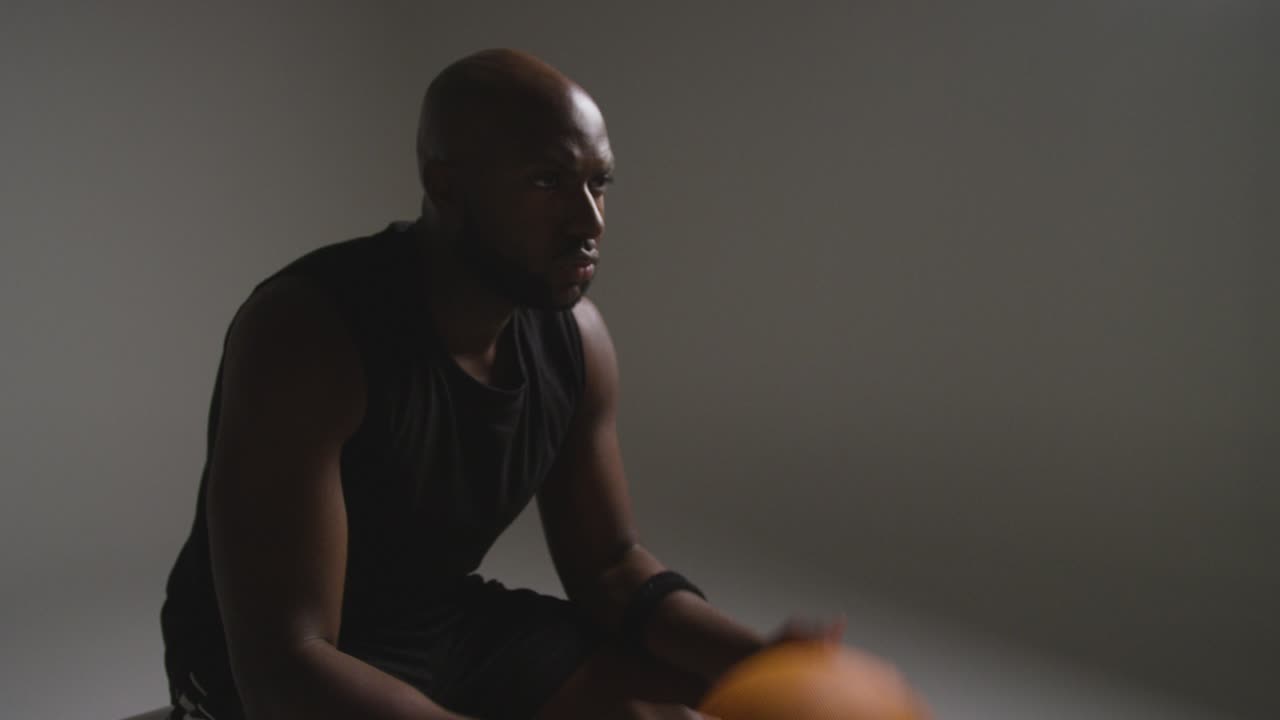 Studio Shot Of Seated Male Basketball Player With Hands Holding Ball 3