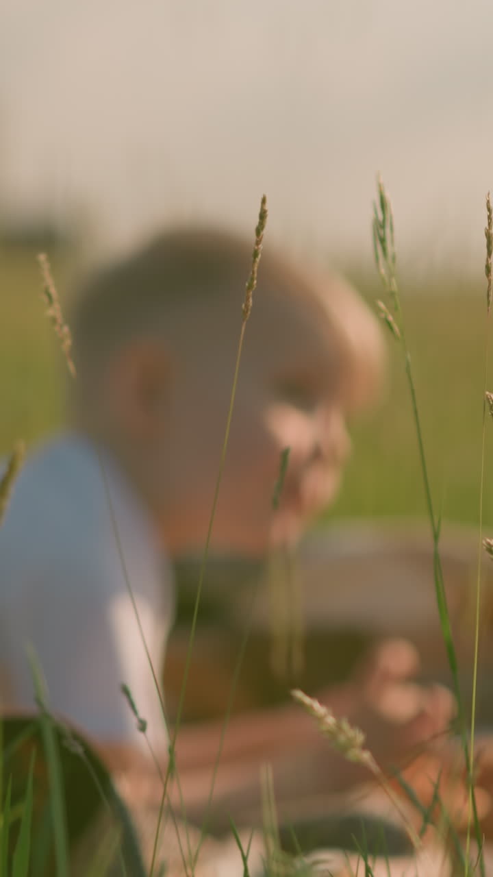 색 셔츠를 입은 두 아이가 잔디에 은 스카프에 앉아있는 흐릿한 이미지.  한 이 그 사이에 배치되어 시골 환경에서 평화로운 야외 순간을 포착합니다.