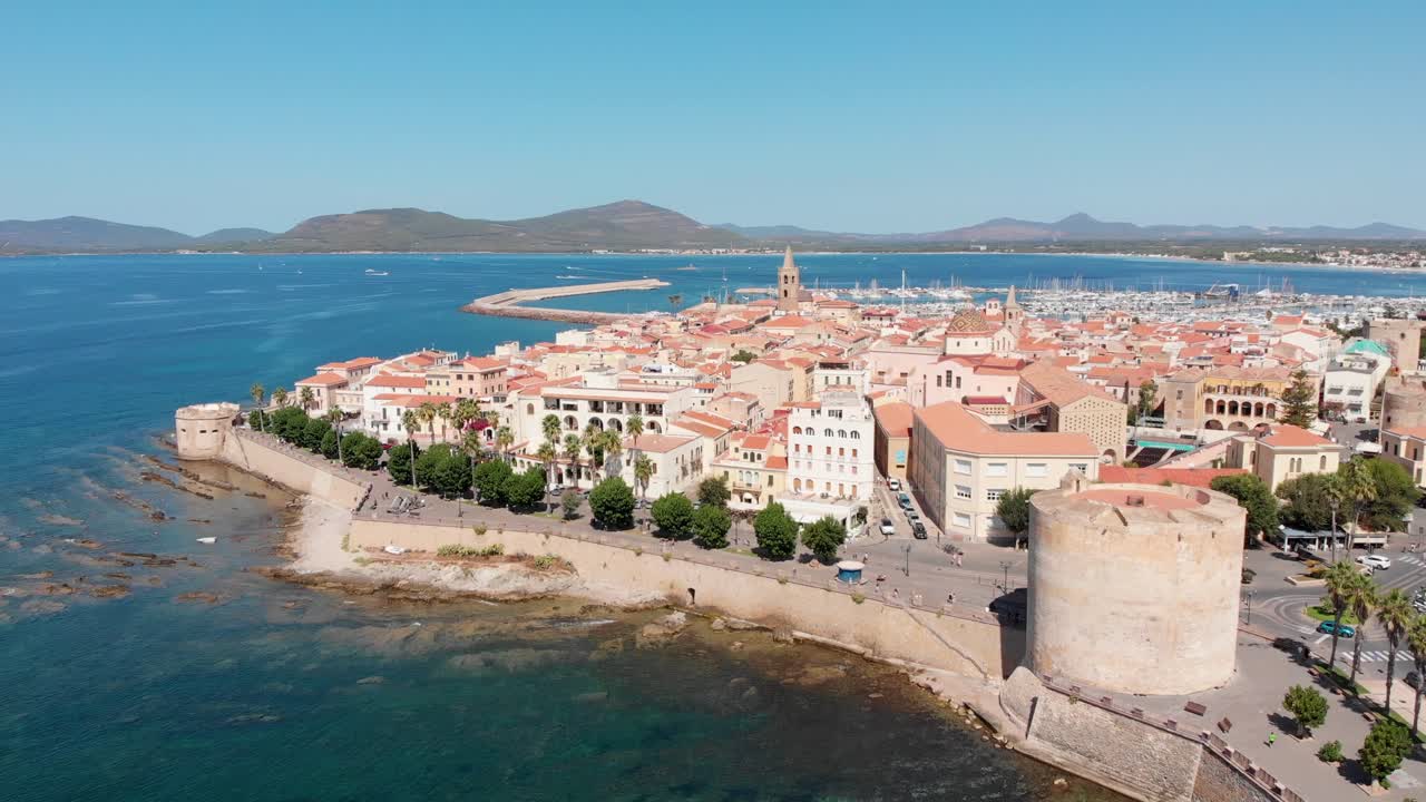 Ripresa aerea: drone in ascesa che rivela il centro storico di Alghero e la costa mediterranea.