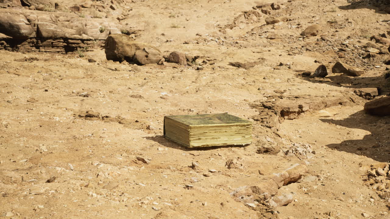 Ancient book resting on dry desert ground surrounded by rocks and sand
