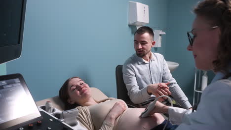 pregnant woman having ultrasound scan at the gynecologist office while loving husband holding her hand 7