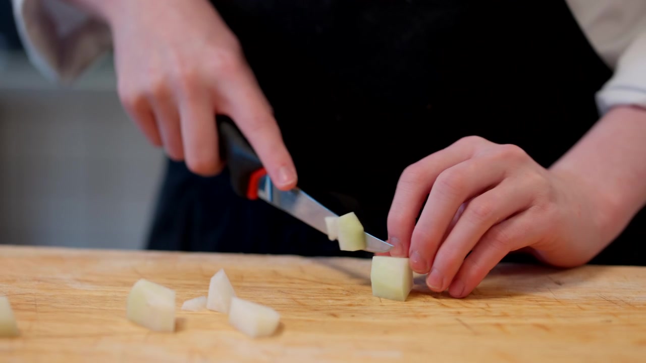 A chef slicing potatoes with precision on a cutting board during food preparation, breaking into cubes