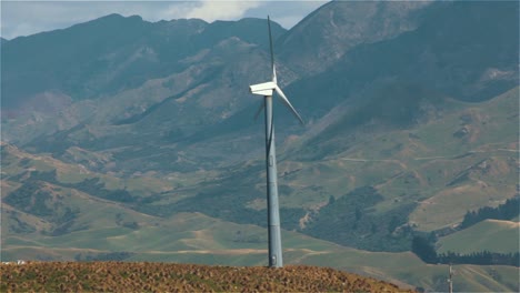 Molino-De-Viento-Girando-Con-Montañas-En-El-Fondo,-Turbina-Eólica-De-Energía-Eólica-Generando-Electricidad,-Futuro-De-Energía-Verde---Disparo-Constante