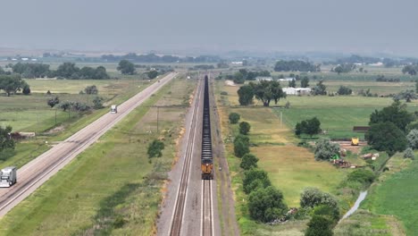 Static-aerial-view-of-freight-train-moving-along-tracks-parallel-to-highway