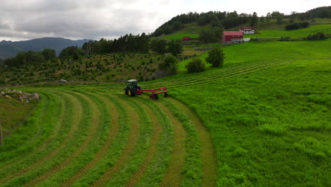 Drone-following-a-tractor-driving-on-pasture-and-cutting-grass-for-silage,-animal-feed