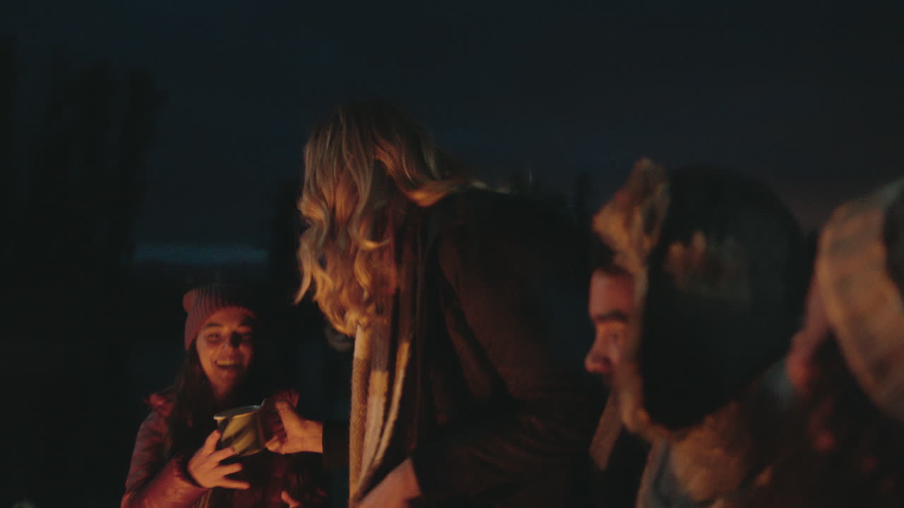 amigos felices acampando sentados junto a una fogata en el bosque por la noche charlando bebiendo chocolate caliente asando malvaviscos compartiendo calidez disfrutando de una aventura al aire libre