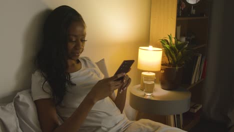 Pareja-En-Casa-Por-La-Noche-Acostada-En-La-Cama-Con-Una-Mujer-Mirando-El-Teléfono-Móvil-2