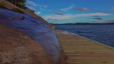 toma de un muelle de madera a lo largo de una pendiente rocosa junto a un lago tranquilo durante todo el día en un lapso de tiempo