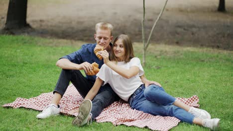 A-girl-and-a-guy-feed-each-other-a-croissant-at-a-picnic-as-a-couple.-romantic-date-happiness