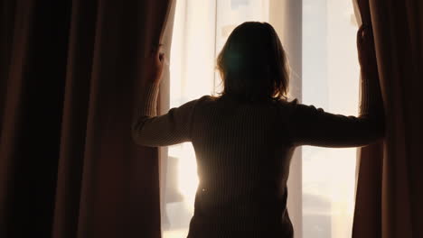 Woman-looks-out-the-window-and-holds-the-curtains-with-her-hands