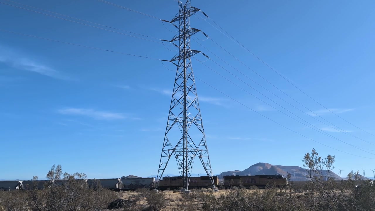 A freight train moves steadily beneath tall power lines across the arid Mojave Desert. Ideal for transportation and infrastructure themes.