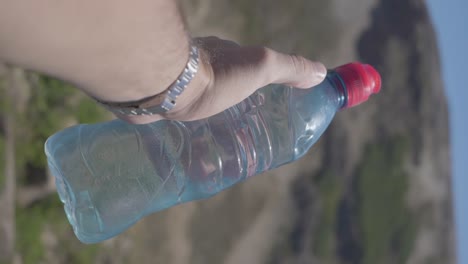 un hombre de vacaciones sosteniendo una botella de agua que muestra una panorámica en cámara lenta de colinas, bosques y un lago en la patagonia, argentina