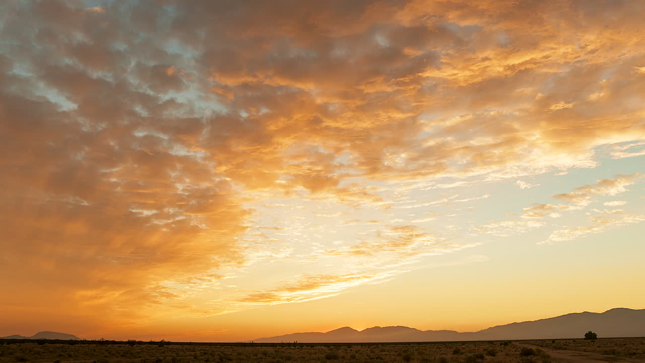 빠르게 움직이는 구름은 모하비 사막 풍경 위로 석양이 빛나면서 황금색에서 분홍색으로 빛납니다.