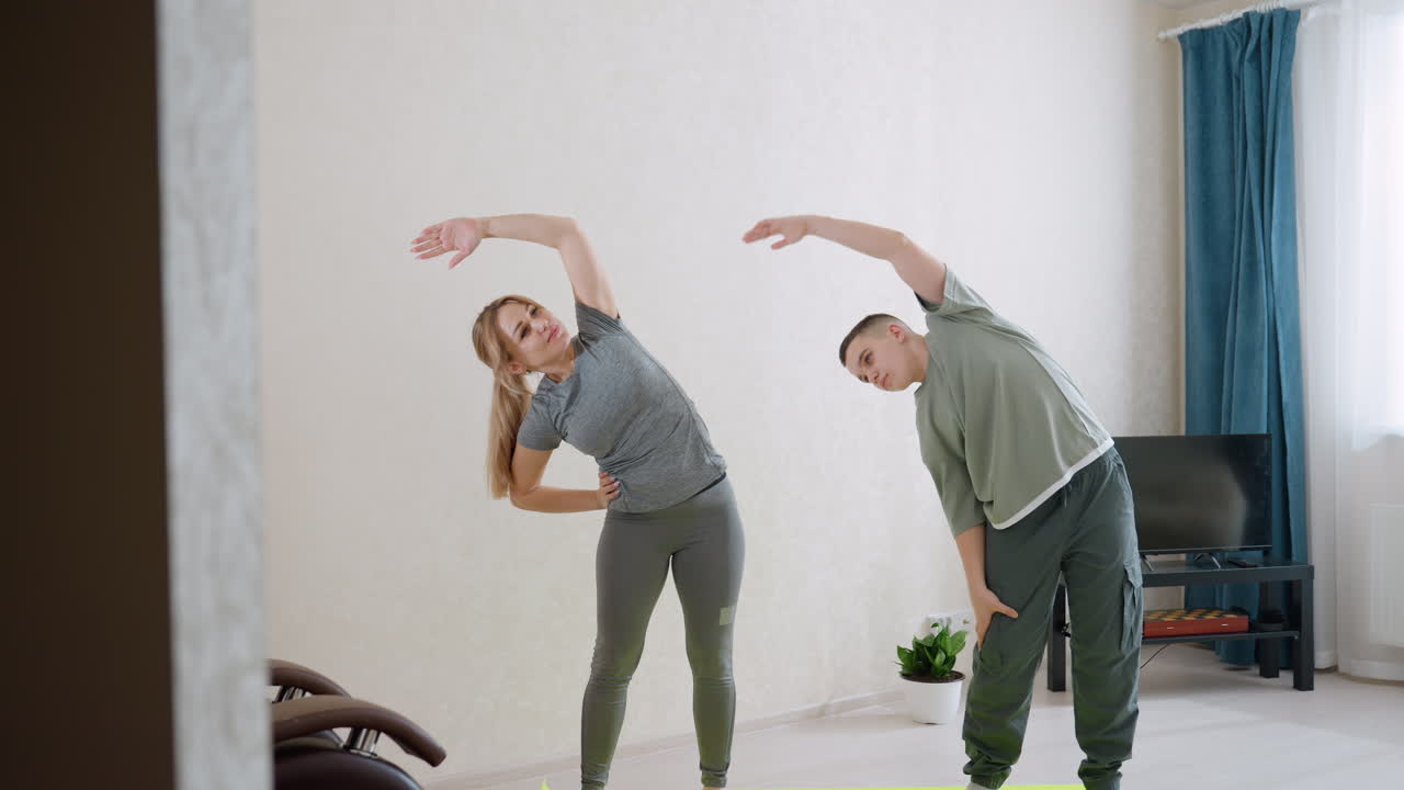 실내 운동 세션에서 팔을 옆으로 뻗으며 건강한 라이프스타일, 균형, 절제, 동기 부여를 보여주는 여성과 소년. 미소, 팀워크, 지지적인 상호 작용이 함께해요.