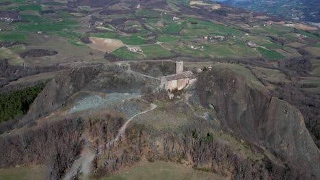 Aerial-footage-of-Pietra-Perduca,-volcanic-rock,-church-set-at-top-stone-immersed-in-countryside-landscape,-cultivated-land-in-Val-Trebbia-Bobbio,-Emilia-Romagna,-Italy