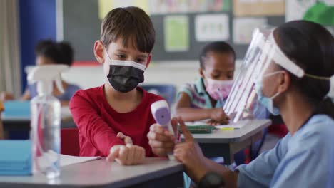 trabajador médico diverso enseñando a un escolar cómo medir la temperatura, todos con máscaras faciales,