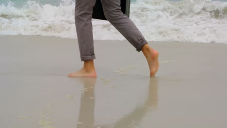 sección baja de hombre de negocios caminando descalzo con maletín en la playa 4k
