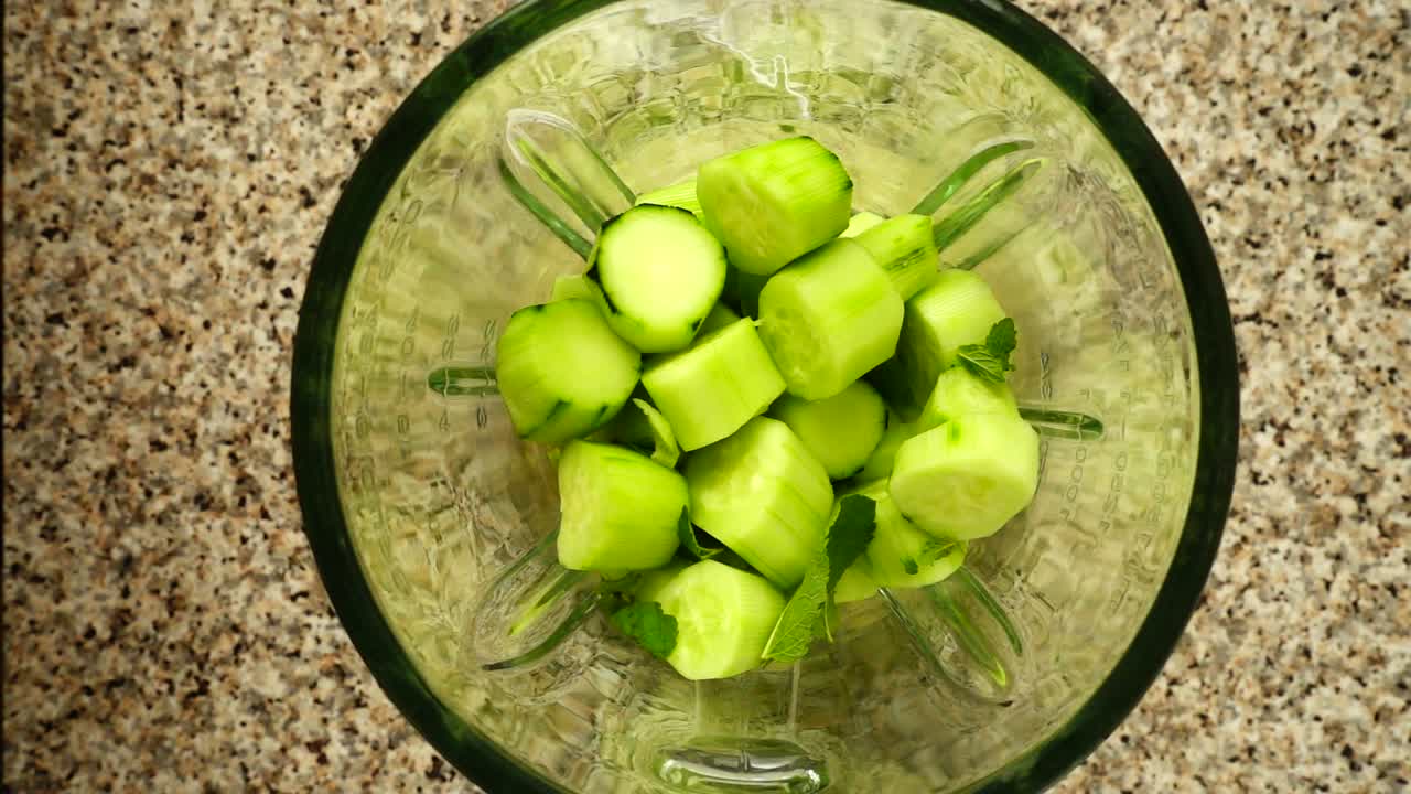 Mentha leaves fall in a blender bowl on pieces of a cucumber. Slow motion. Shooting in kitchen. Top view