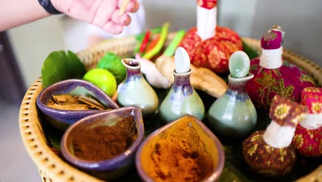 a hand arranges herbal ingredients and oils for a traditional thai massage, showcasing vibrant colors and natural elements