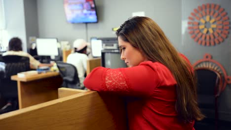 Woman-in-red-shirt-leans-against-cubical-and-observes-coworkers