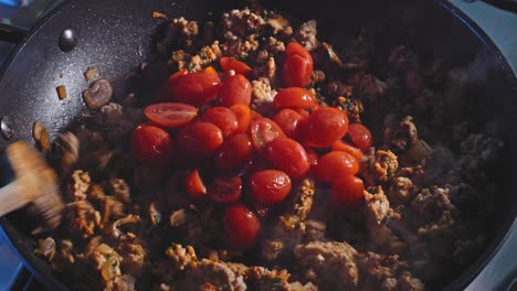 adding fresh cherry tomatoes to ground turkey meat cooking in pan