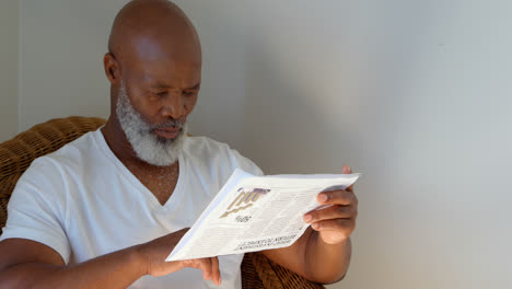 front view of black mature man reading newspaper at home 4k