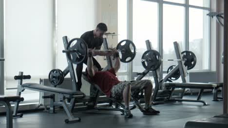 man getting bench press help from trainer in a gym