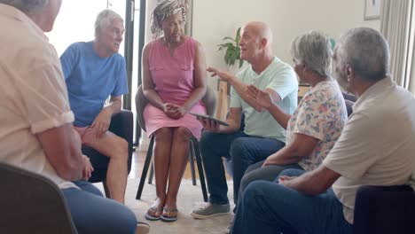 diverse seniors and male therapist with tablet talking in therapy session, unaltered, slow motion