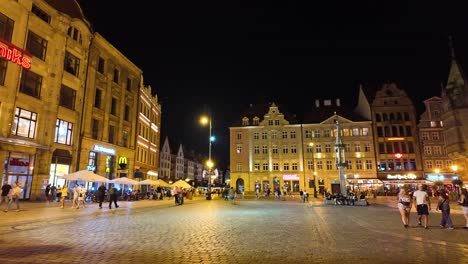 lively ambiance of wroclaw market square at night, featuring illuminated historic buildings, bustling cafes. pan left shot