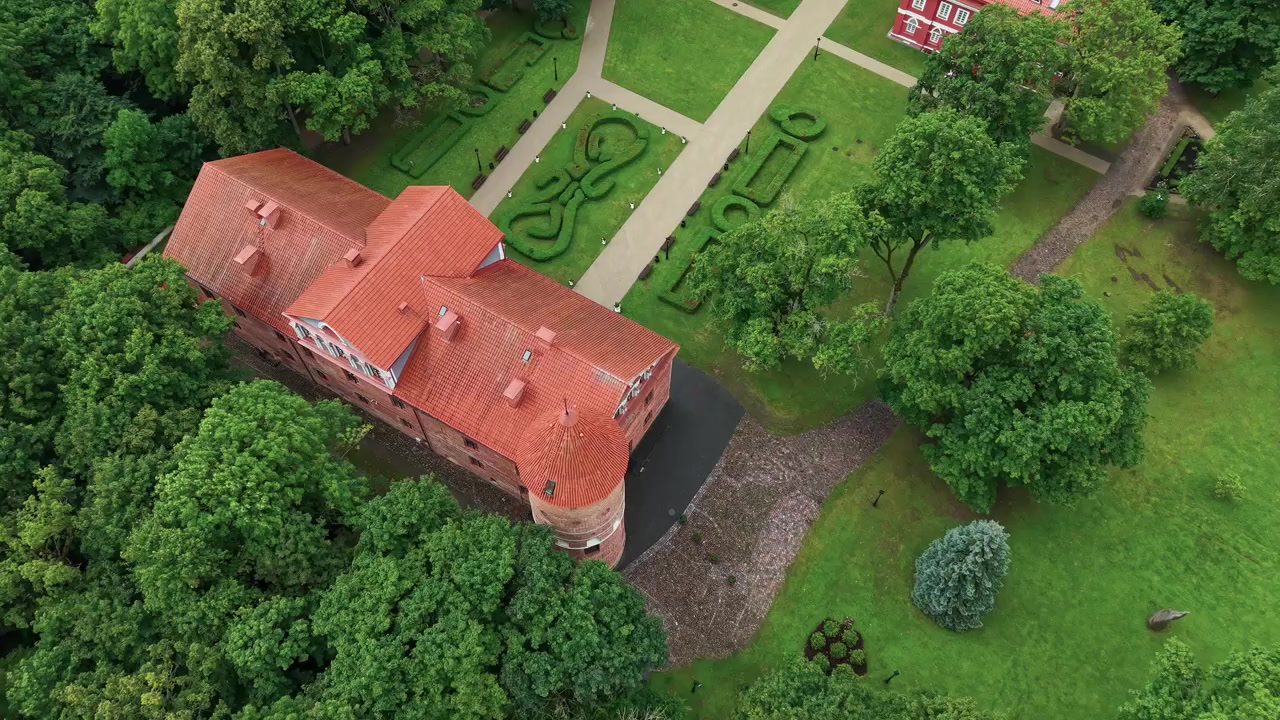 Splendide riprese aeree con drone rivelano il Castello di Raudondvaris immerso in un vivace parco verde, con giardini curati, tetti storici in tegole rosse, sentieri alberati e suggestiva illuminazione estiva