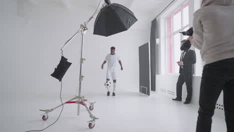 afro-american footballer is posing for camera of photographer in studio showing kick-up skill