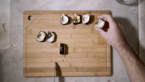 lasso di tempo di vista dall'alto verso il basso su due mani sulla tavoletta di taglio in legno sul bancone della cucina tagliando un rotolo di sushi a pezzi