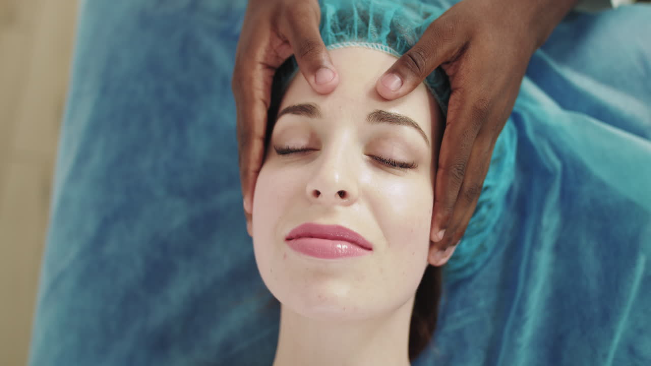 Masseuse die hoofd- en gezichtsmassage geeft aan haar ontspannen en mooie jonge vrouwelijke cliënt die geniet