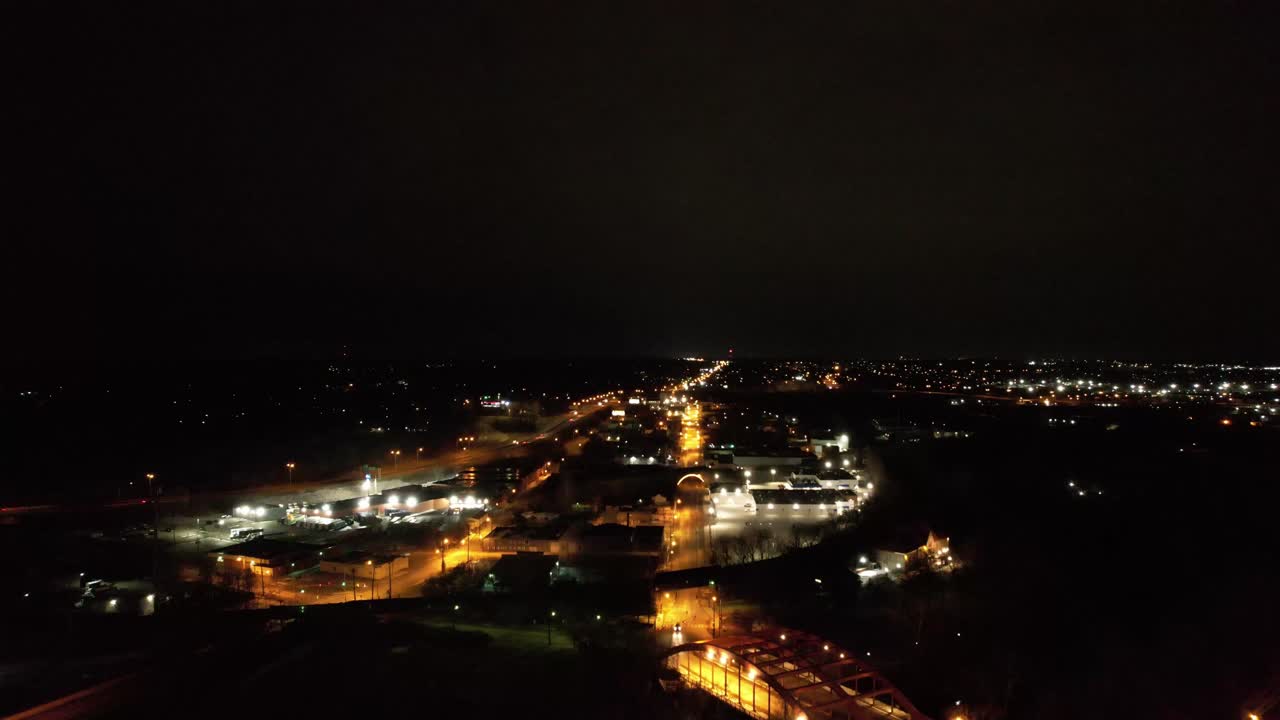A drone flies above Youngstown, Ohio at night, capturing glowing streetlights along a major road that cuts through the city under a dark sky.
