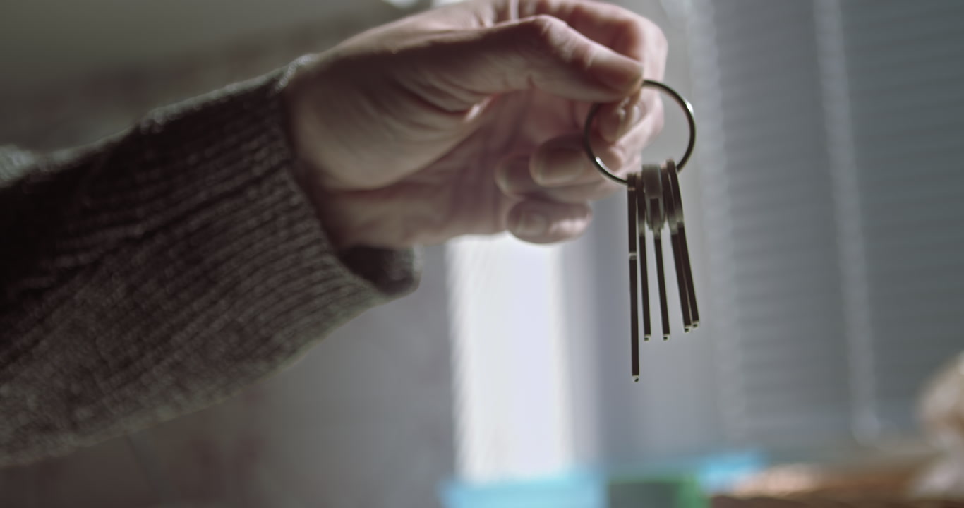 An outstretched arm holds a set of house keys in a sunlit interior. Ideal for real estate marketing, home buying concepts, and mortgage lending advertisements.
