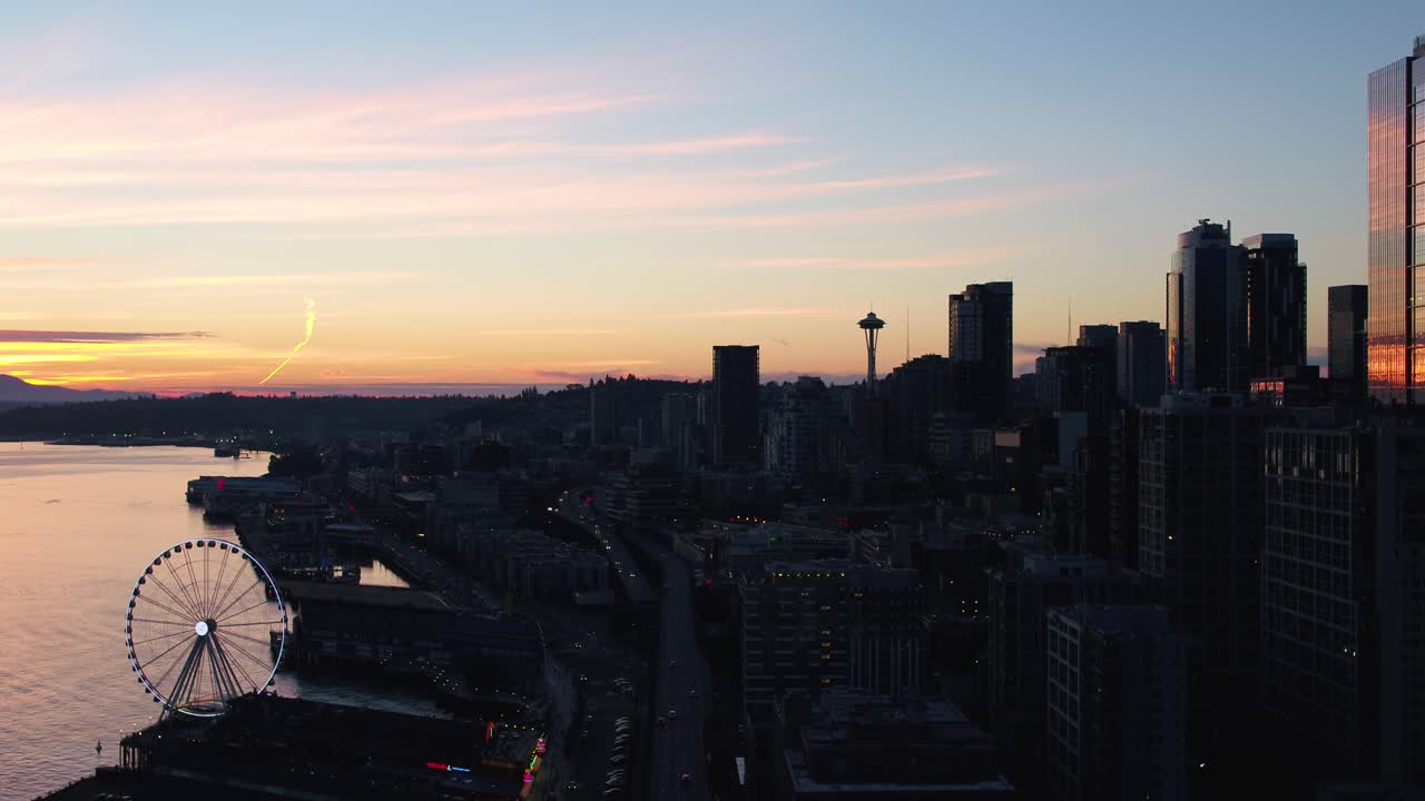 Aerial pushing towardf Seattle's downtown corridor at sunset. Silhouettes of the big wheel and the Space Needle are easily visible.