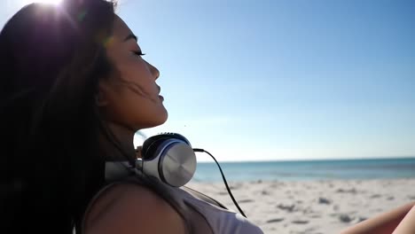 a serene moment by the beach: a young woman enjoys the ocean breeze with headphones, immersing in the sounds of nature under the bright sky