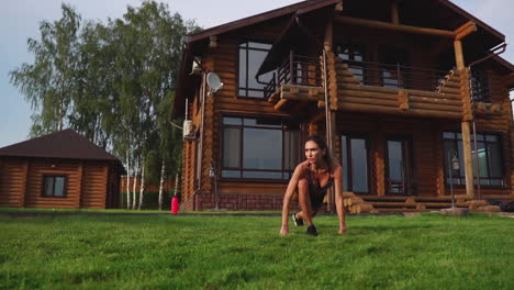 mujer delgada y hermosa en ropa deportiva en el fondo de la casa en el césped realiza saltos para el entrenamiento cardiovascular y la quema de grasa