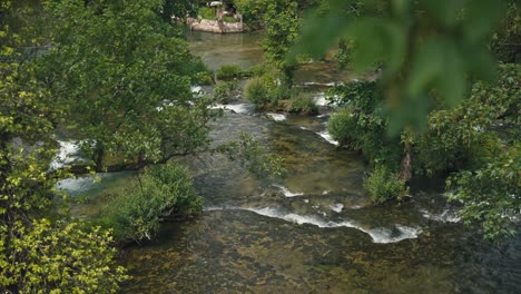 Vista-De-Las-Aguas-Claras-Y-Poco-Profundas-Del-Río-Slunjčica-Que-Fluyen-Sobre-Rocas-Y-Están-Rodeadas-De-Exuberante-Vegetación-En-Rastoke,-Croacia