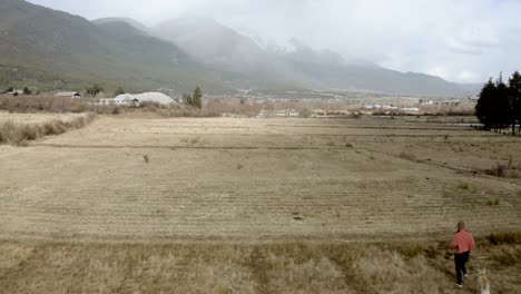 Free-woman-and-dog-running-through-remote-grass-field,-Chinese-mountains,-aerial