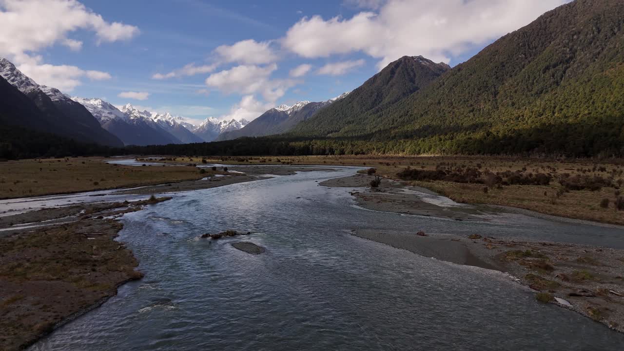 Volo radente sul torrente tra montagne innevate coperte di nuvole bianche in direzione di Milford Sound, Southland, Nuova Zelanda