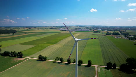 aerial high-angle view of wind turbine spinning on large tower in crops farmland in poland countryside on sunny day