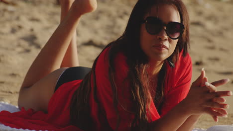 young latino woman on beach sunbathes in golden sunshine licks her lips and smiles