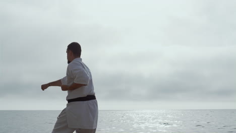 atleta practicando karate de pie en la playa del océano. luchador de judo practicando ataque.