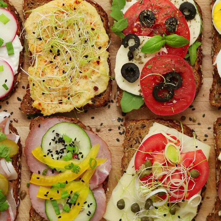 Diversi tipi di panini colorati serviti su un tagliere di legno con condimenti di verdure.