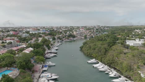 aerial forward over canal of la romana port with boats anchored along river shores, dominican republic